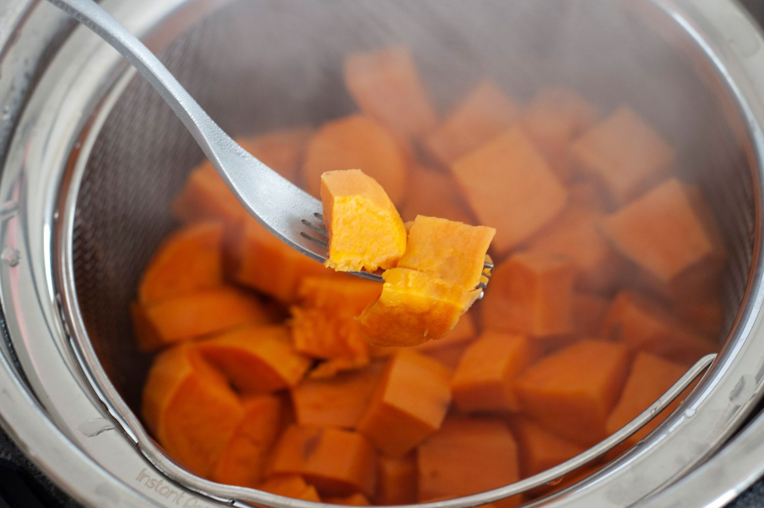 Steamed Sweet Potatoes on a Fork with More in a Metal Steamer Basket in the Background