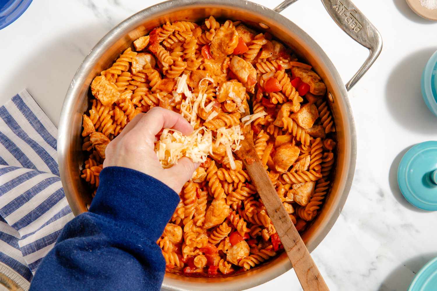 hand sprinkling shredded pepper jack cheese onto pasta mixture in pan for One-Pan Chicken Fajita Pasta