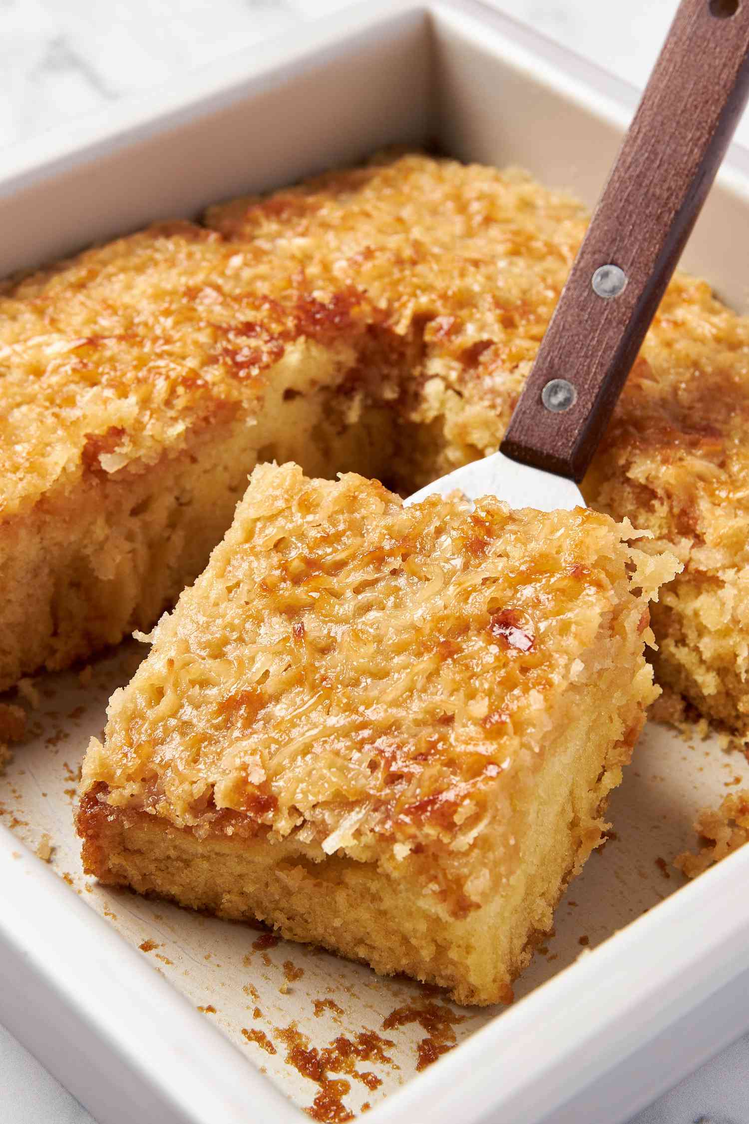 Lazy daisy cake slice on a spatula leaning up against more cake in the baking pan