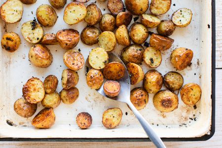 Oven Roasted New Potatoes on a Tray with a Spoon Scooping Some Potatoes