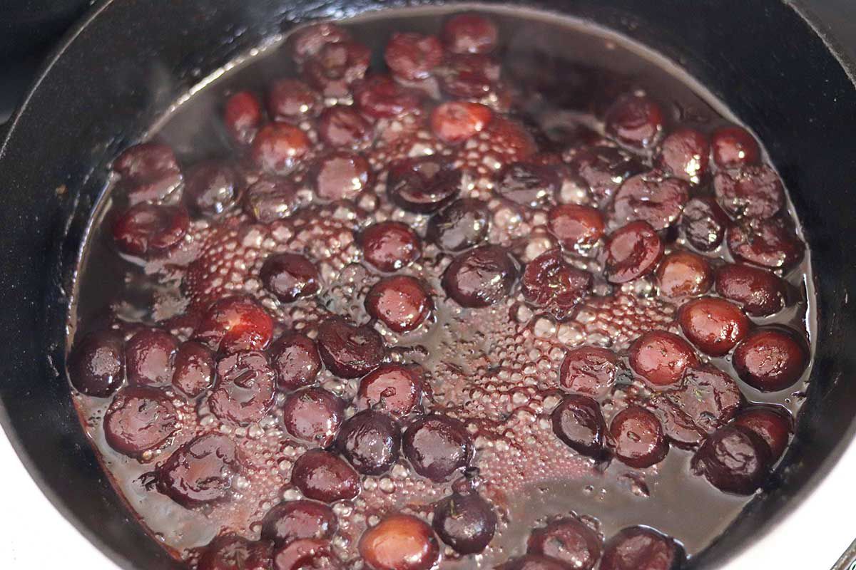 Cherry sauce bubbling in a cast iron skillet for fried pork chops.