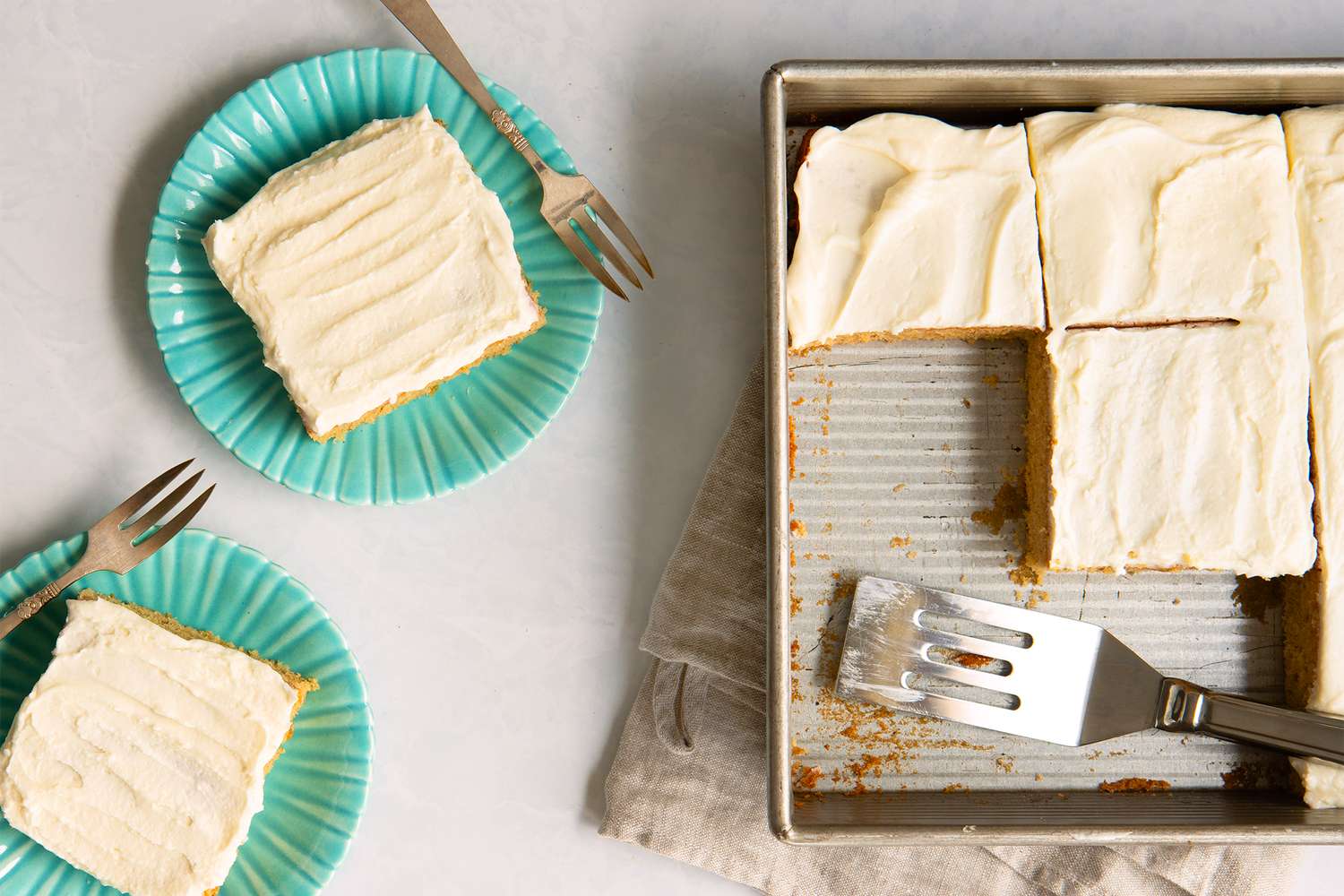 A baking tray with a frosted sheet cake and slices served on teal plates with forks