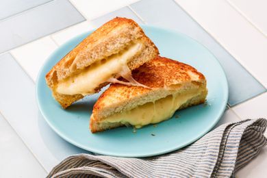 Sheet Pan Grilled Cheese Sandwich Cut in Half and on a Light Blue Plate Next to a Table Napkin