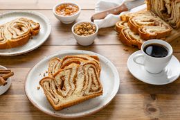 Plates with Slices of Povitica Surrounded by a Cutting Board with More Slices, Small Bowls of Ingredients (Pecans, Cinnamon, etc), and a Cup of Coffee