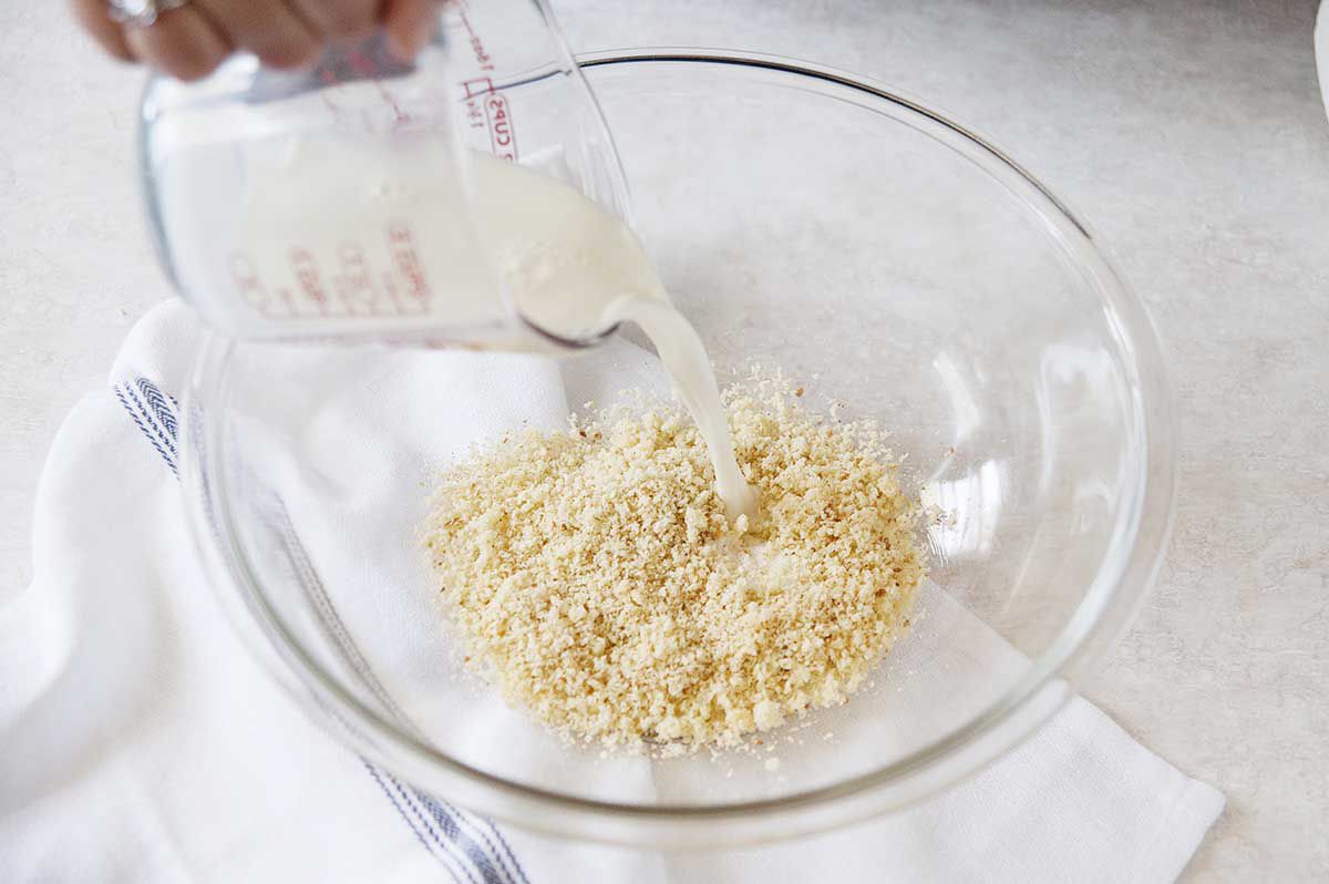 Adding milk to a bowl of breadcrumbs to make meatballs.