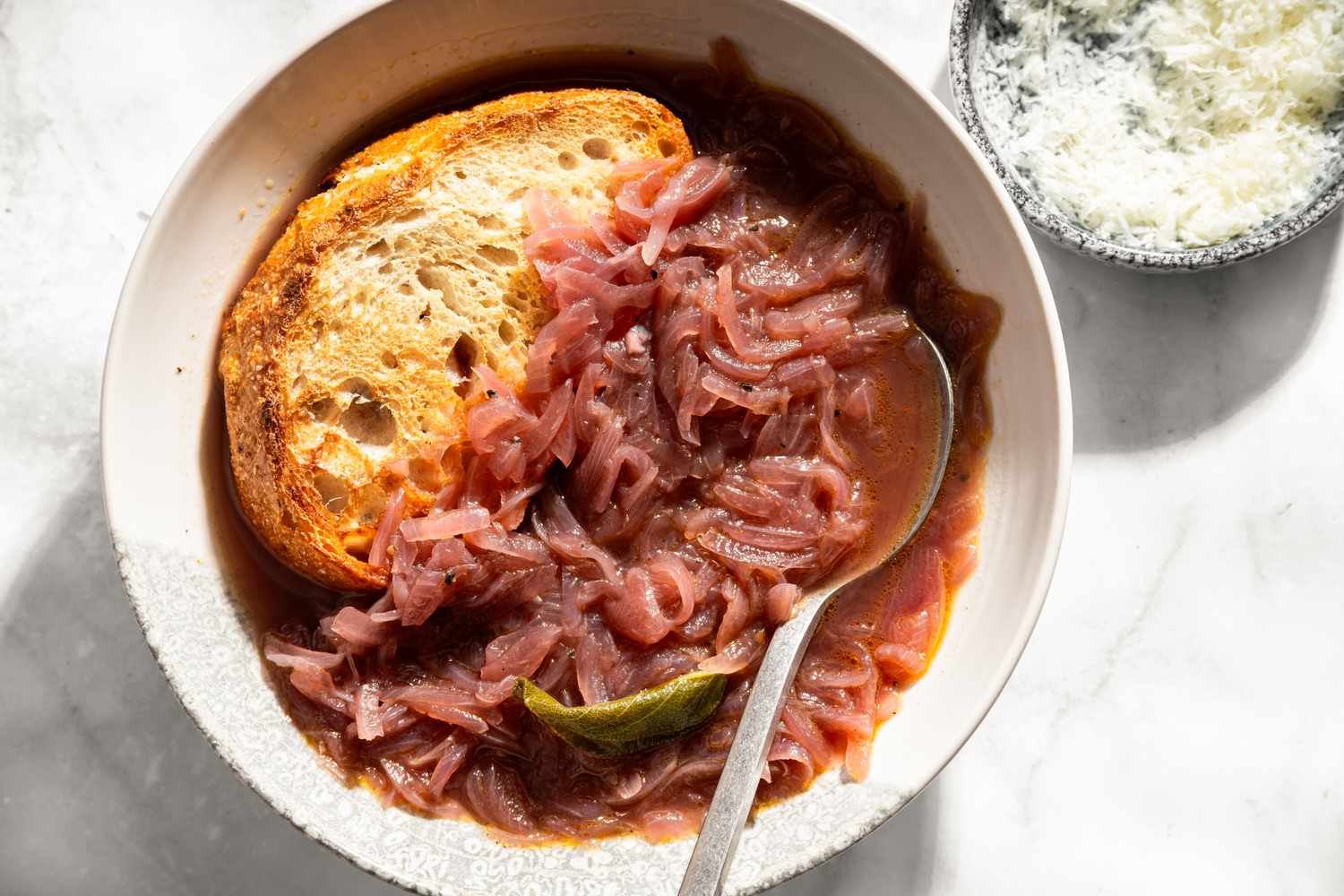 A bowl of Tuscan onion soup with a slice of bread and a spoon garnished with grated cheese