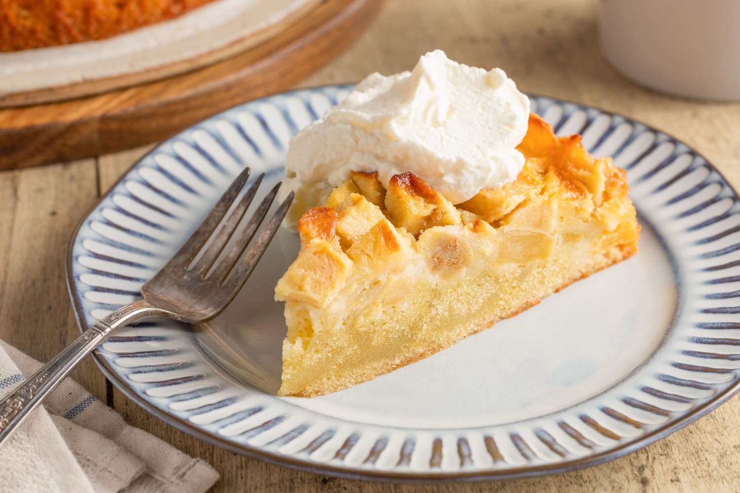 slice of Easy French Apple Cake topped with whipped cream on a dessert plate with a fork