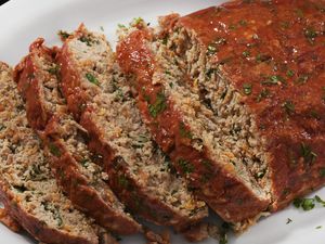 Sliced meatloaf garnished with herbs on a white plate