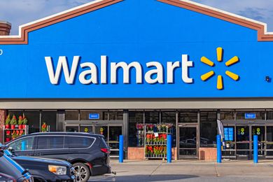 Exterior view of a Walmart store entrance with parked cars in the foreground