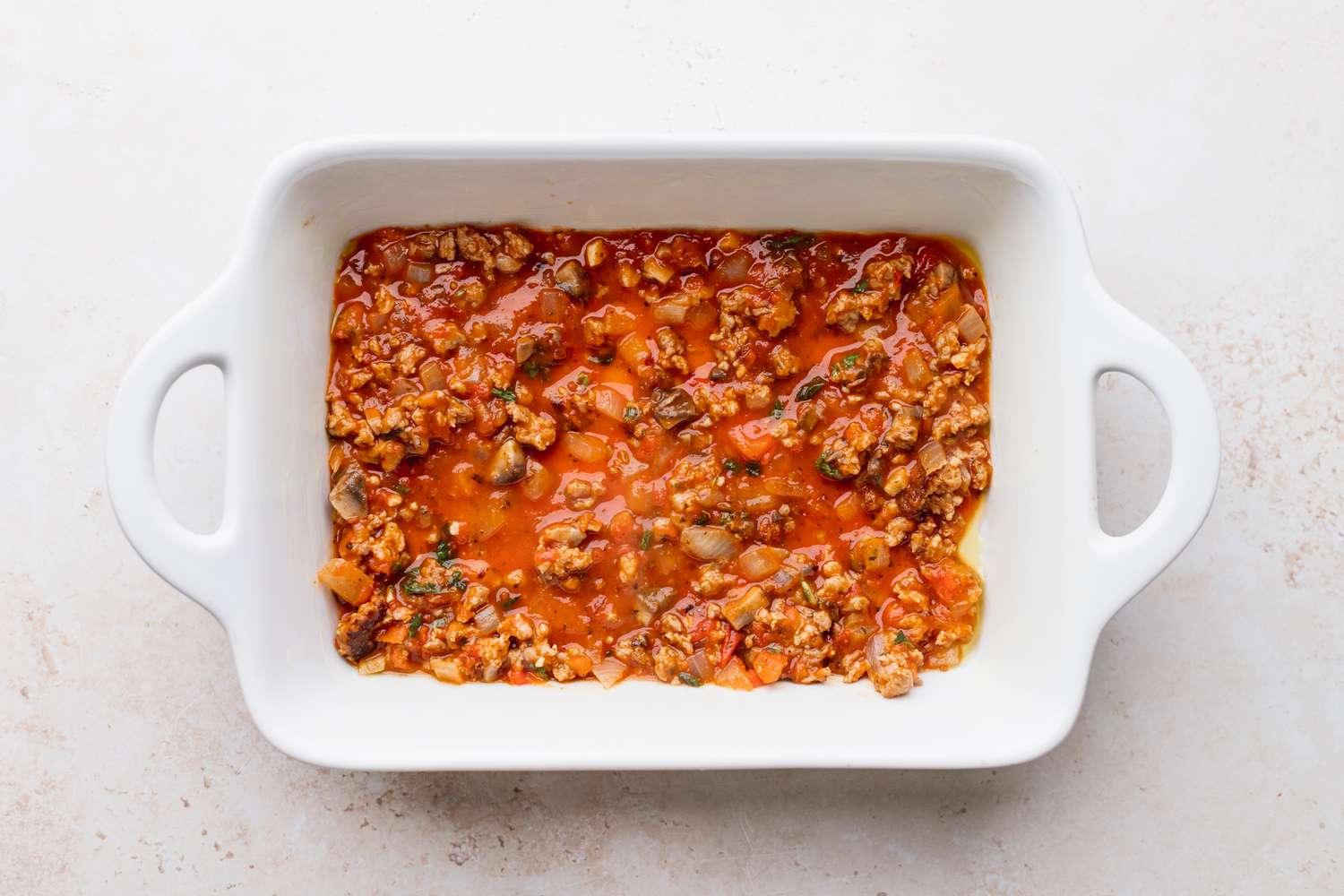 Sauce in a dish showing how to make baked spaghetti