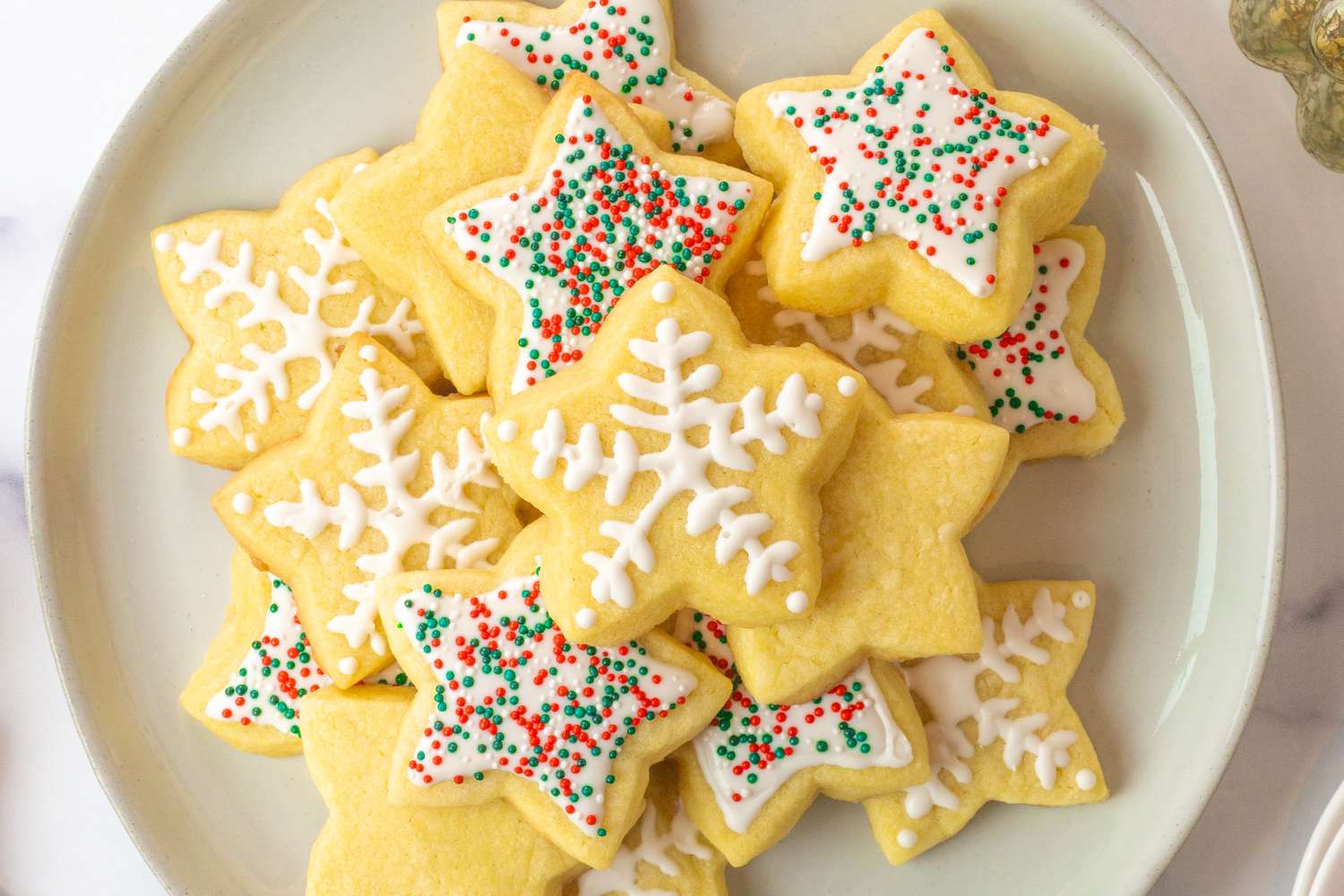 A plate of decorated sugar cookies in shapes of stars featuring icing and festive sprinkles
