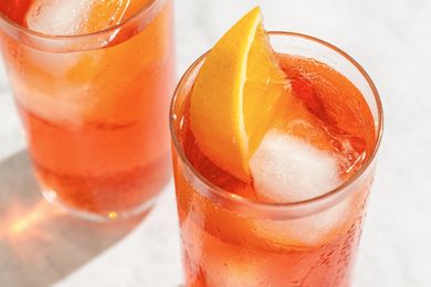 Two glasses of a cocktail garnished with orange wedges