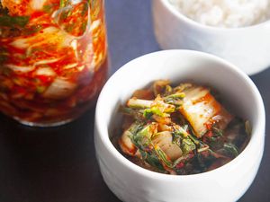 A bowl with easy homemade kimchi is in front of the jar of it and white rice is behind it.