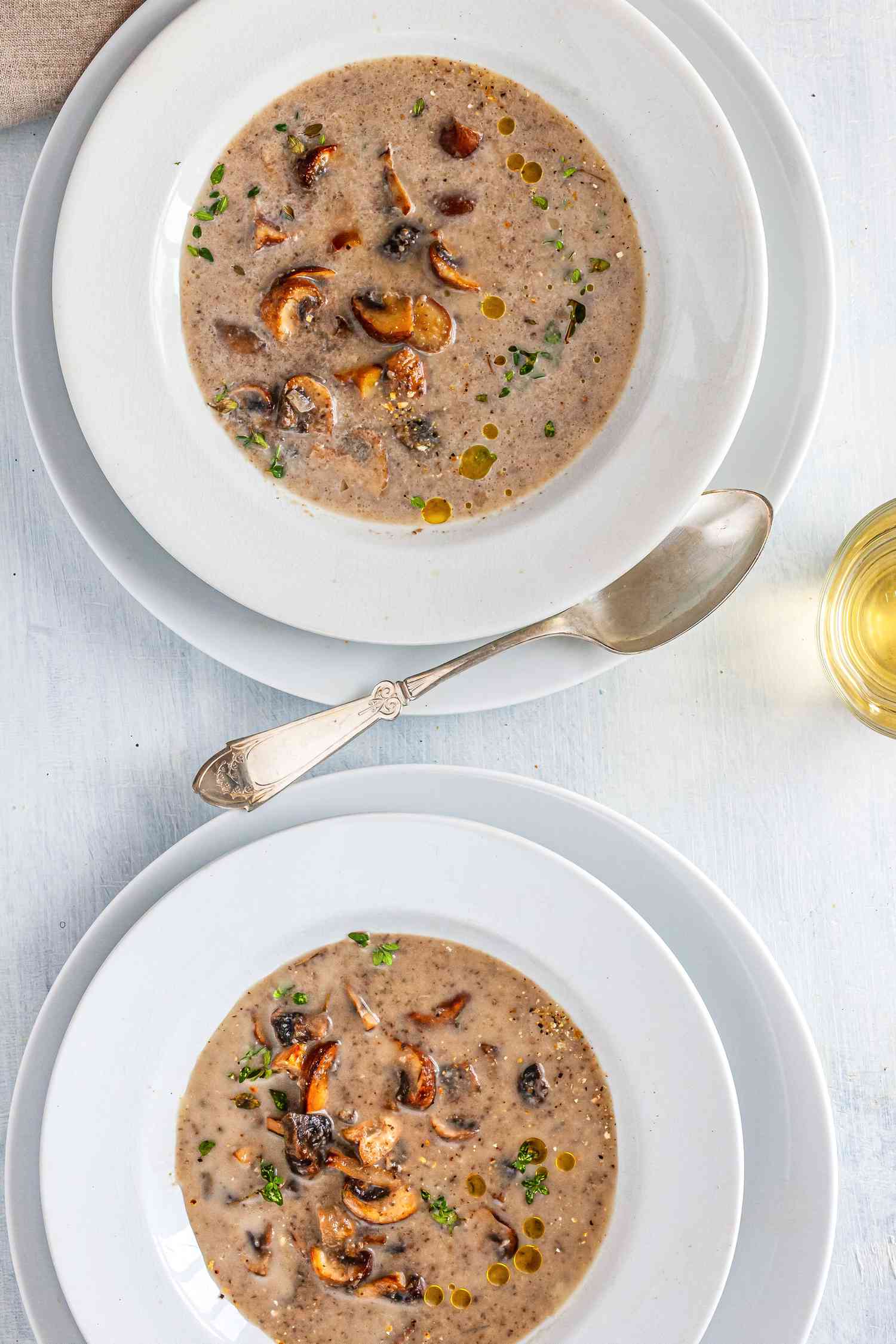 Two bowls fo cremini mushroom and chestnut soup in white bowls with white plates underneath.
