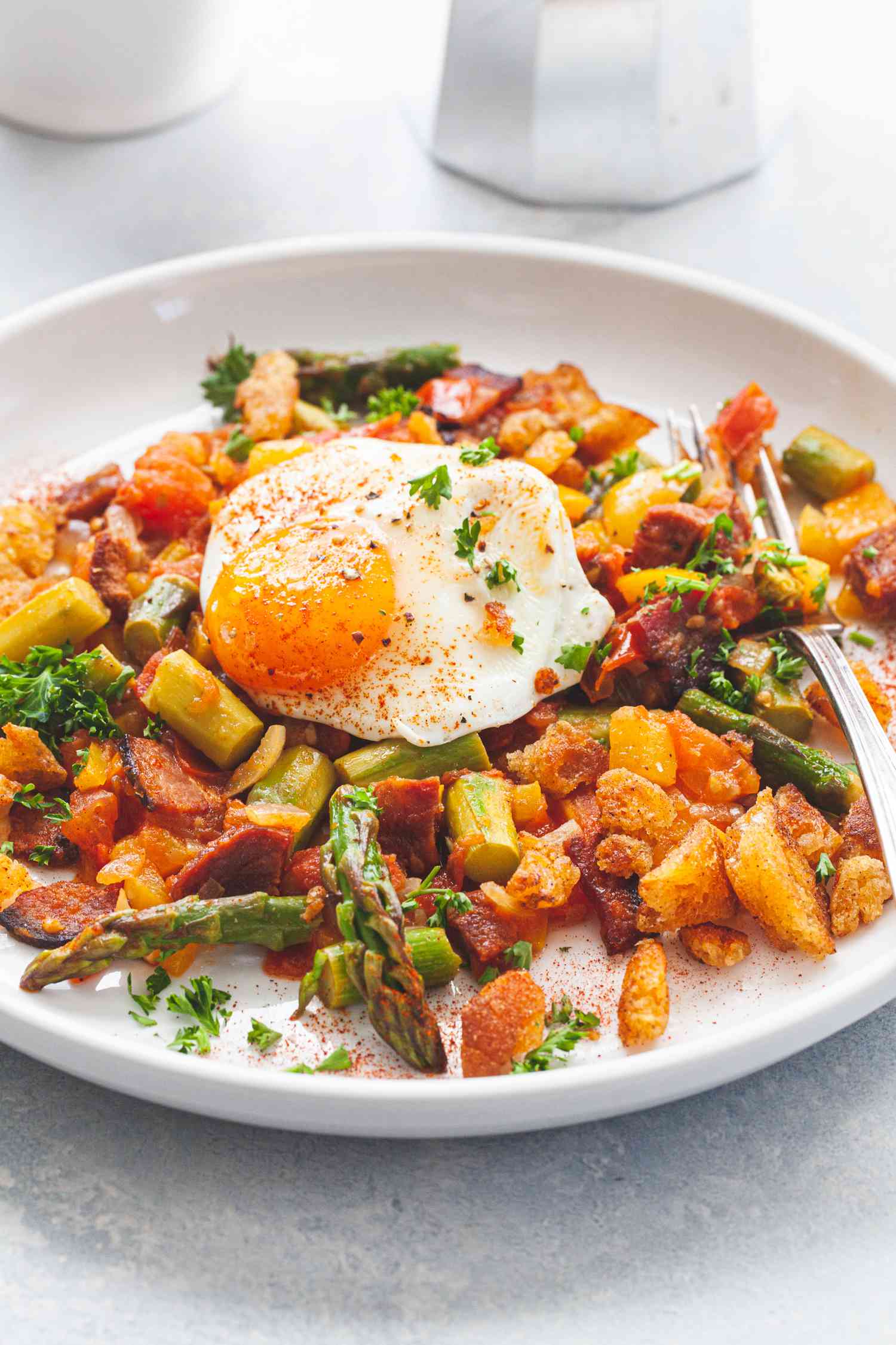 A white plate with Spanish Style Migas with Asparagus, Chorizo, Bacon, and Eggs.