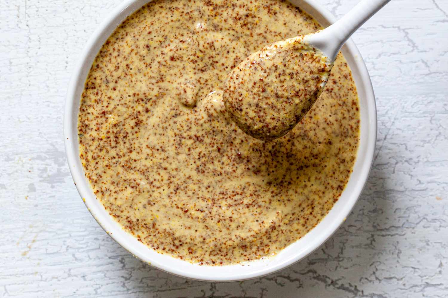 Dijon mustard from scratch in a white bowl with a white spoon.