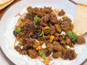 Dish featuring spiced ground meat over a creamy yogurt mixture garnished with mint leaves and served with flatbread