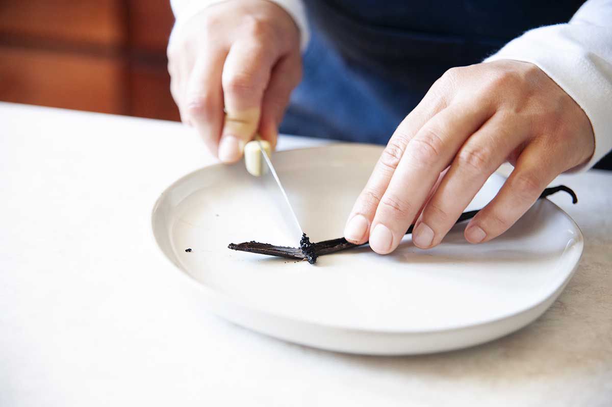 Woman scraping the seeds off a vanilla bean pod.