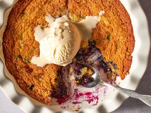 Blueberry corn cake with a scoop of vanilla ice cream on top in a fluted baking dish, served with a spoon