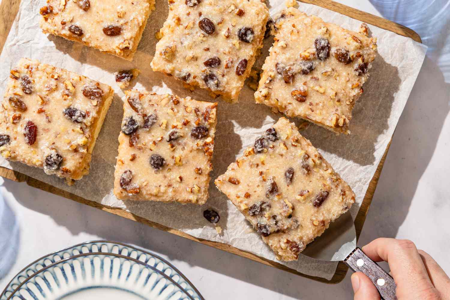 Slices of a nut and raisin cake on a parchmentcovered board with one piece being served