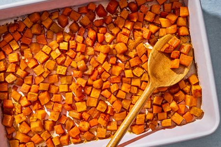 Small cubes of sweet potato, roasted in a baking pan, with a wooden swerving spoon scooping some potato cubes up