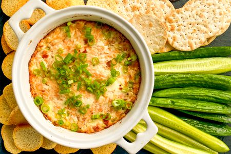 Overhead view of 3-ingredient smoked salmon dip in a white bowl topped green onions and surrounded by crackers, baguette slices and sliced cucumbers