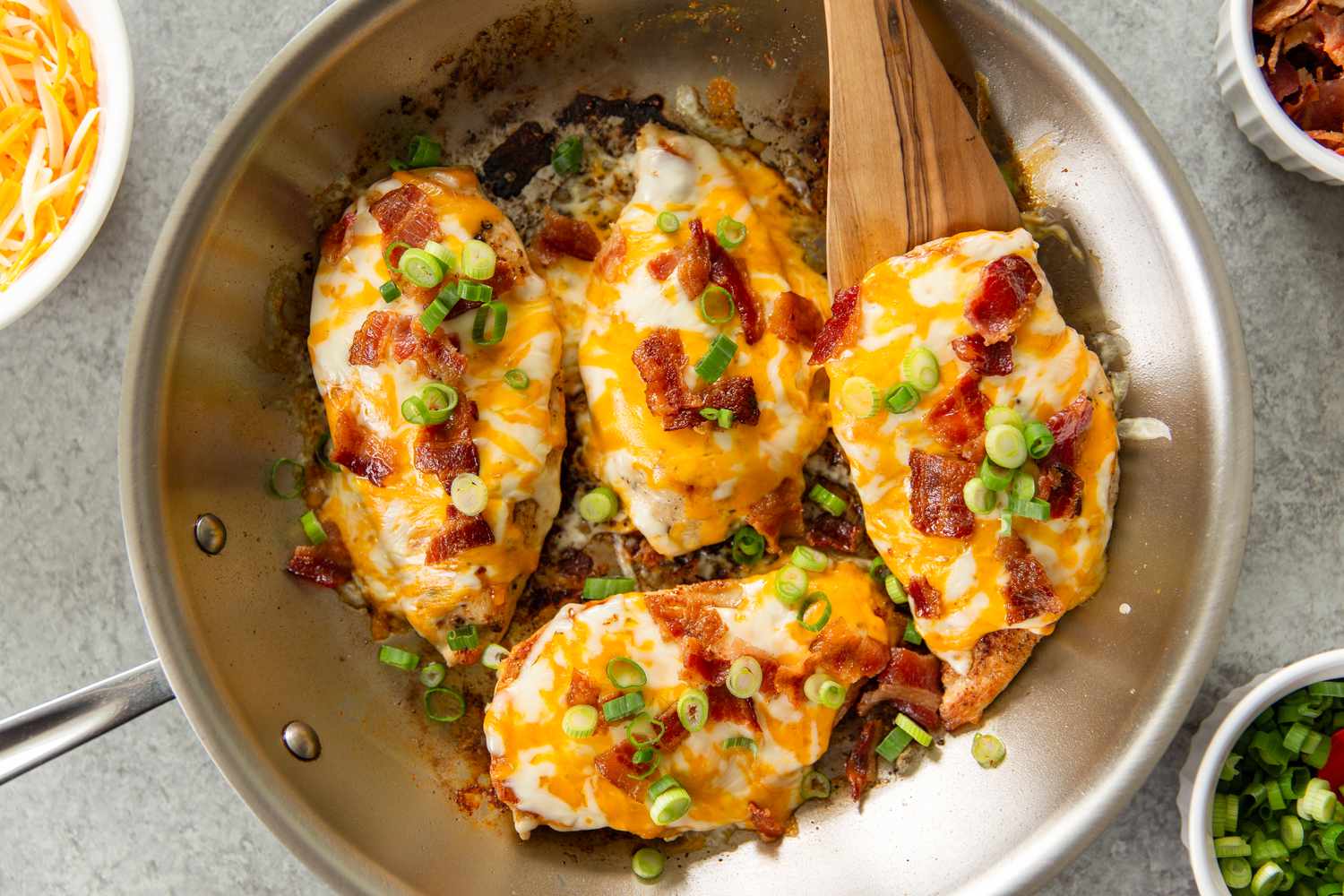 Cooked chicken breasts with cheese, bacon, and green onion in a pan