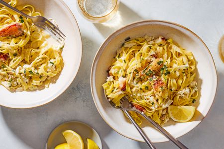 Overhead shot of two bowls with a creamy crab fettuccine pasta, with a lemon wedge and chopped fresh tarragon as garnish