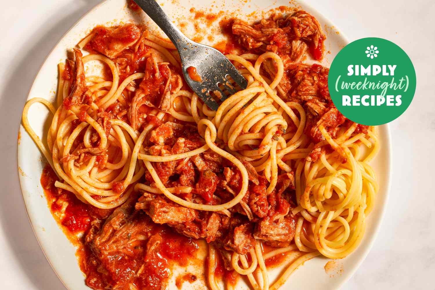 A plate of spaghetti with a meat and tomato sauce partially eaten and a fork placed on top