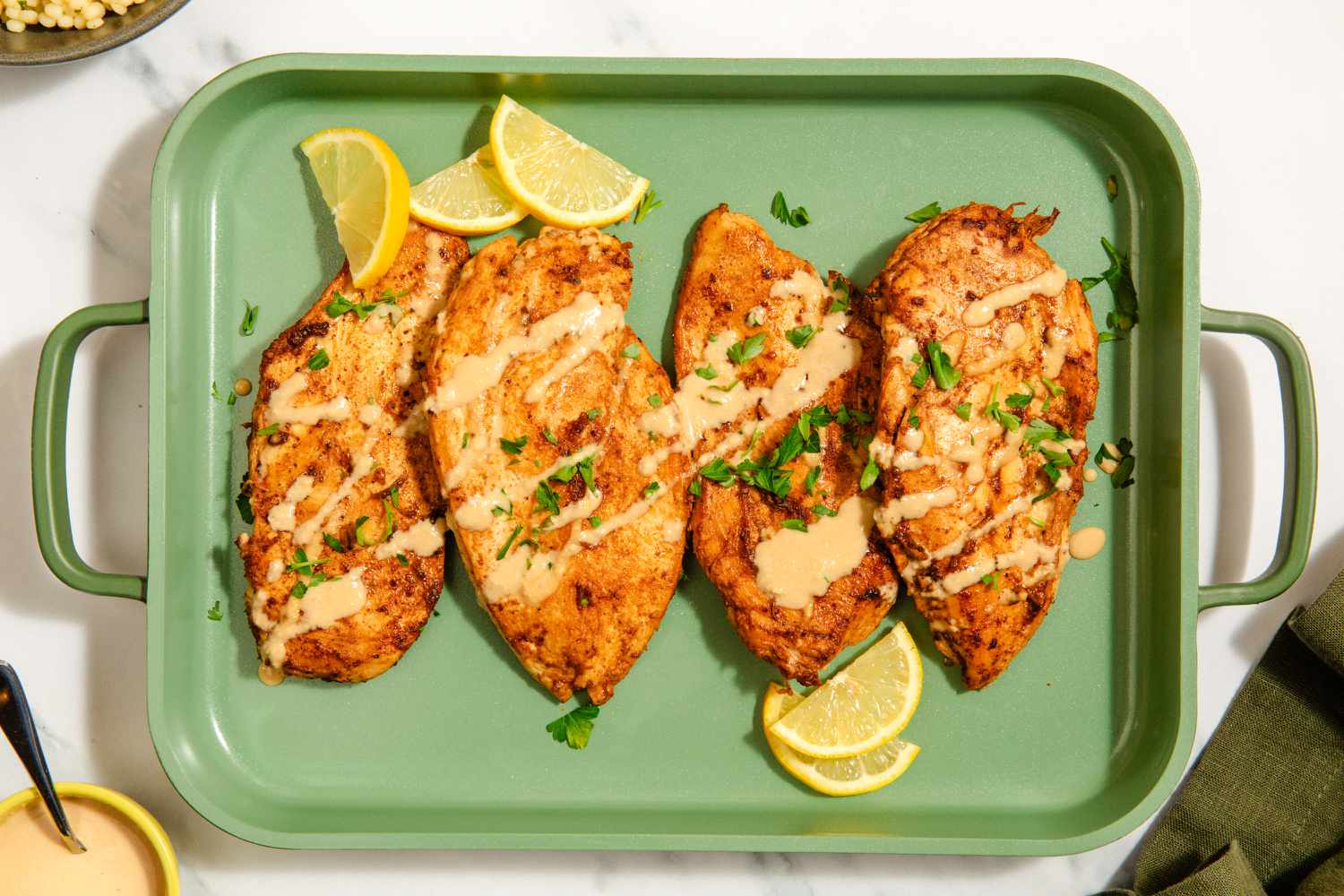 Overhead view of Garlic-Tahini chicken breast cutlets on a green serving tray with lemon slices