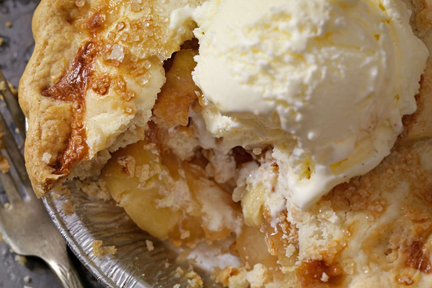 Slice of apple pie topped with a scoop of vanilla ice cream