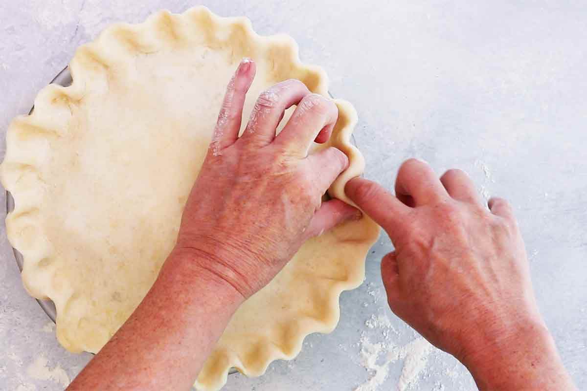 A pair of hands pinching the top curst and merging it into the pie crust 
