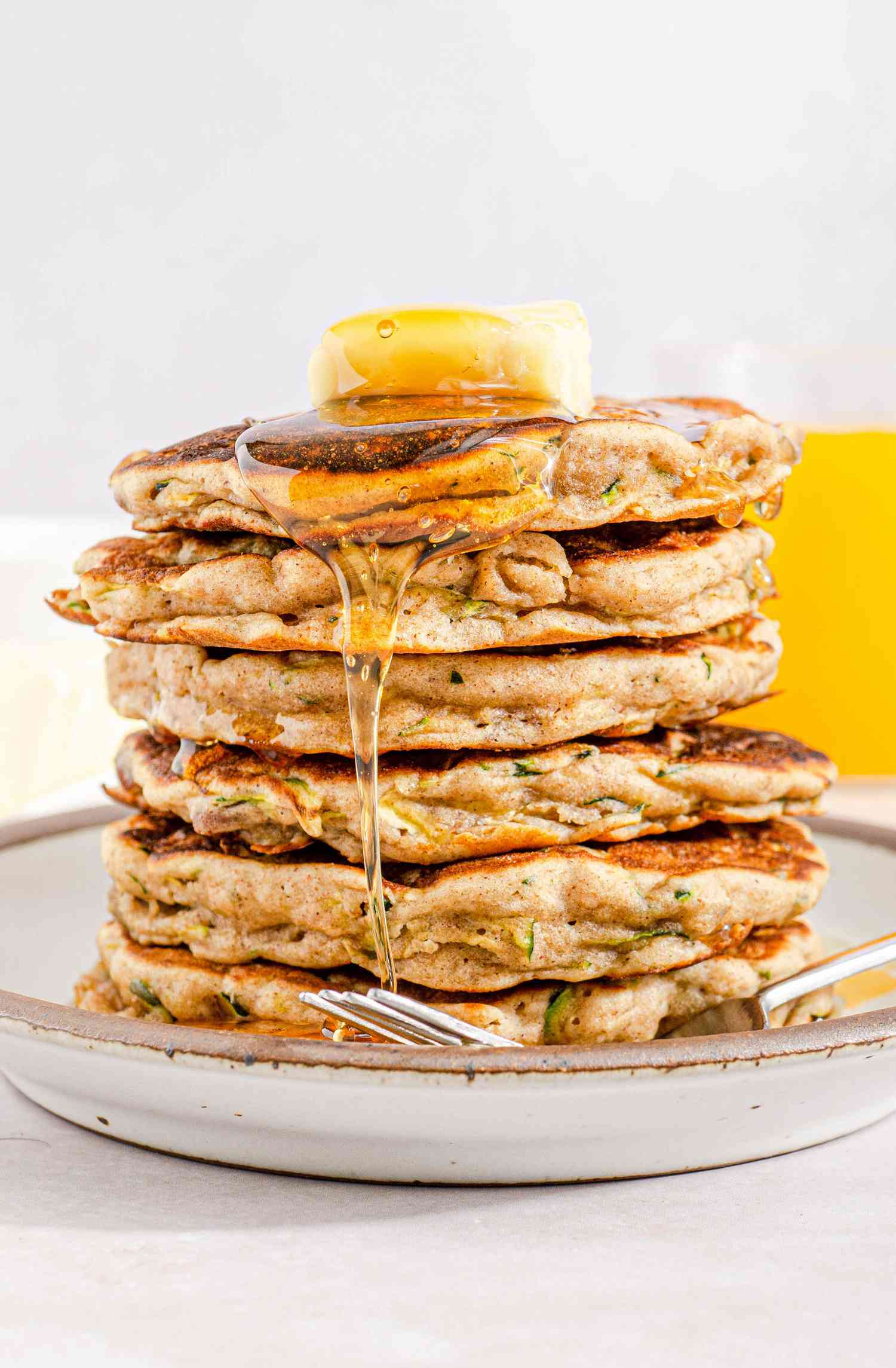 A tall stack of sweet zucchini pancakes on a plate with butter and syrup on top