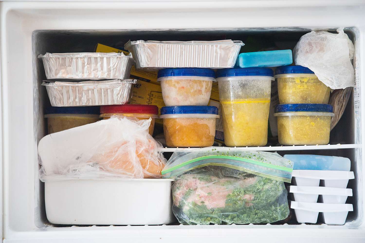 A freezer stocked with various containers and bags of frozen food