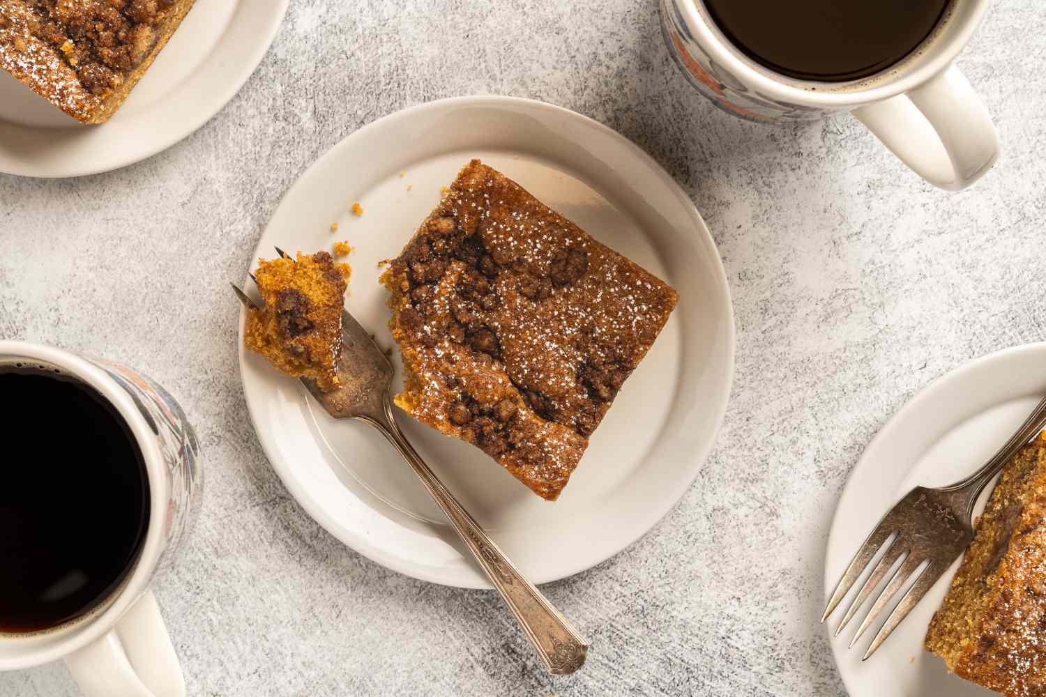 Slices of coffee cake served on small plates with forks alongside cups of coffee
