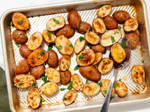 Overhead view of a serving spoon on a metal sheet pan of roasted potato halves topped with parsley