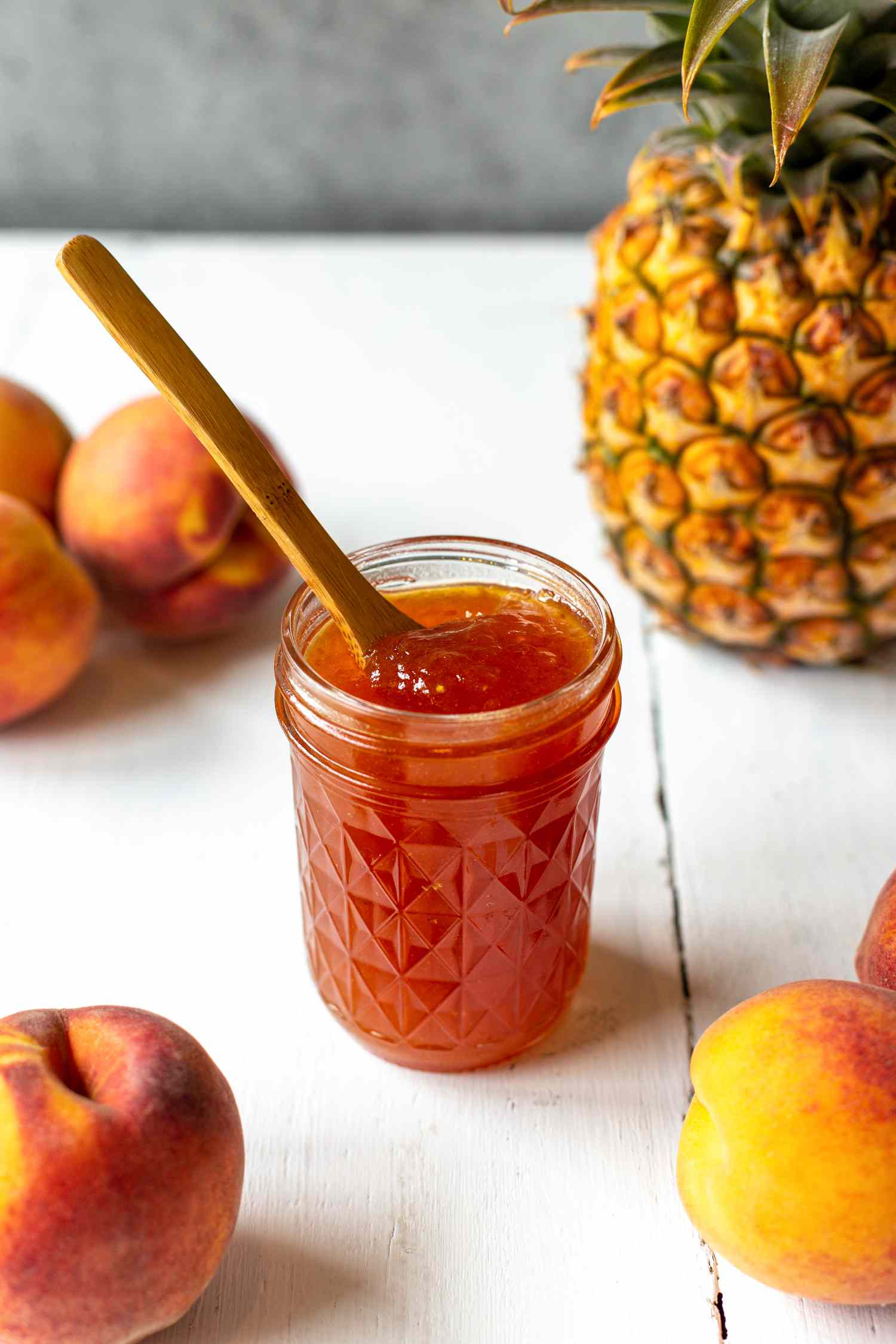 Peach and Pineapple Jam with a Spoon Surrounded by Peaches and a Pineapple