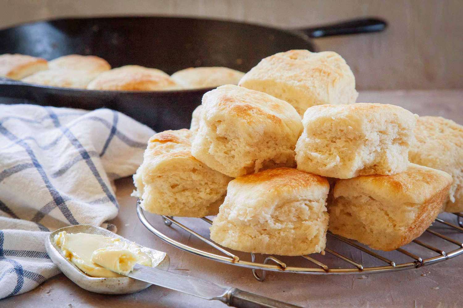 Pile of Angel Biscuits on a Wire Trivet and Next to It, Butter on a Butter Dish. In the Background, More Biscuits in a Pan