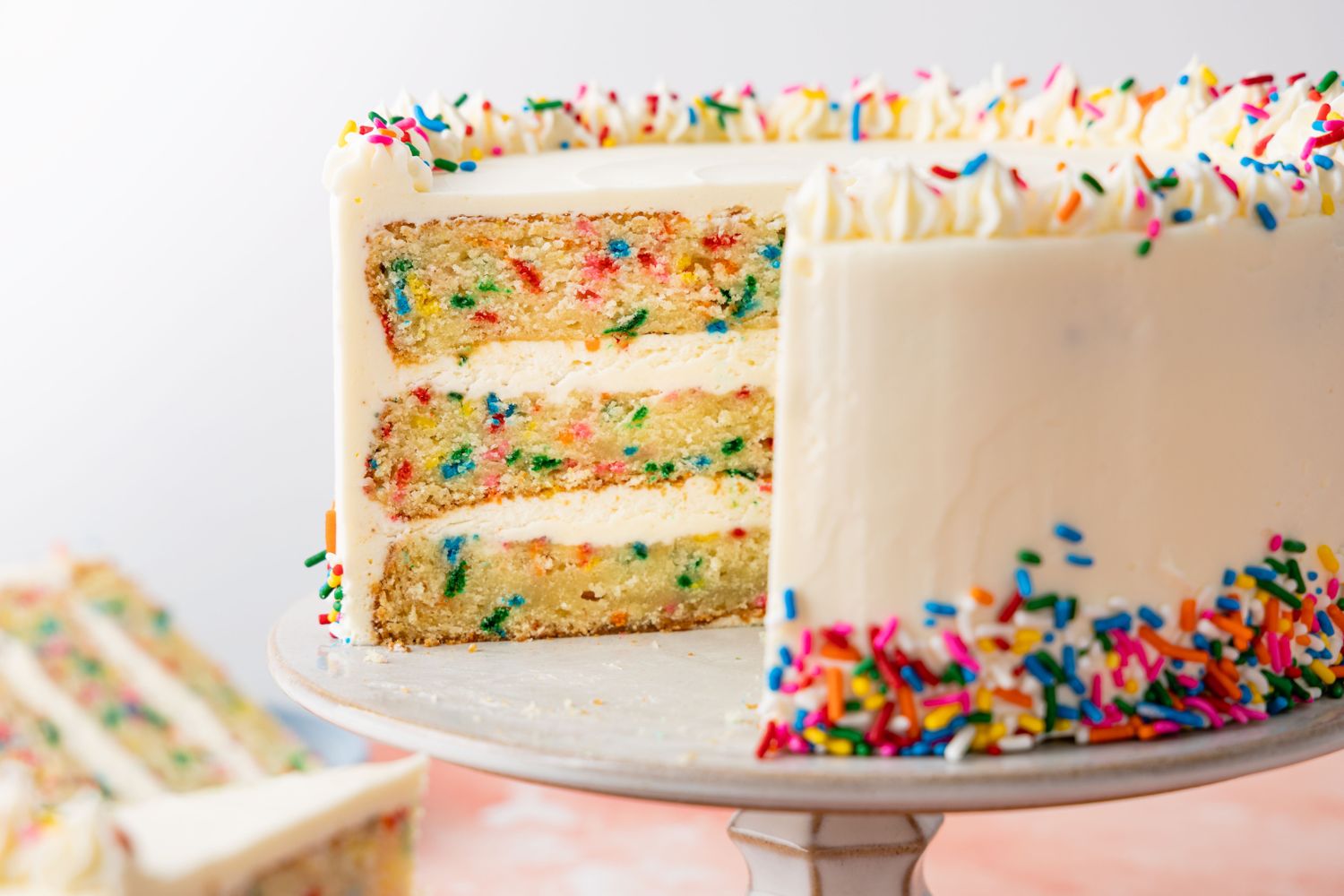 A sliced layer cake with rainbow sprinkles displayed on a cake stand