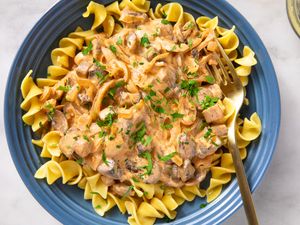 A plate of mushroom stroganoff served over egg noodles garnished with parsley with a fork on the side