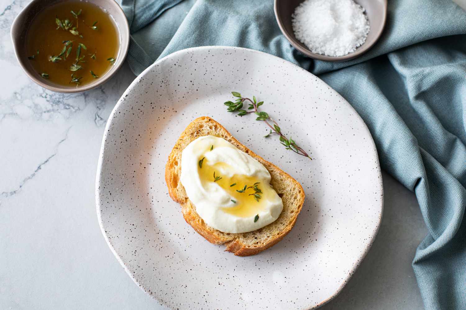 Whipped Ricotta Toast with Lemon-Thyme Honey Drizzle Next to a Bowl with More Thyme Honey and a Bowl with Coarse Salt
