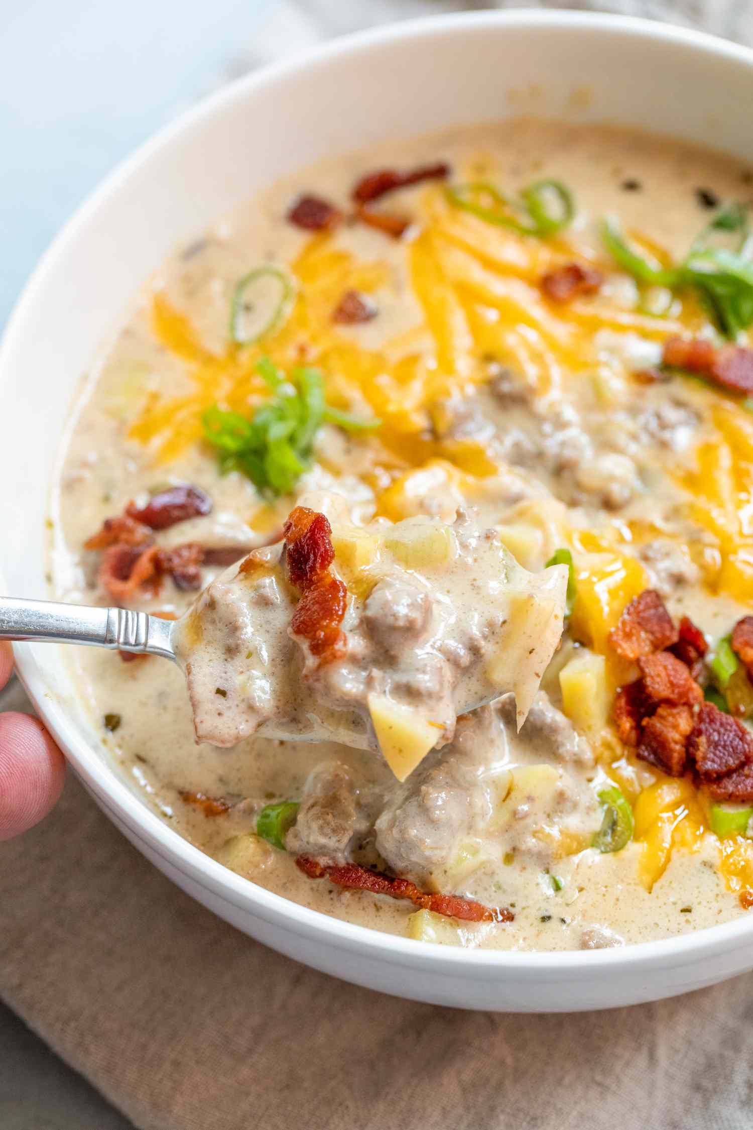 Cheesy bacon cheeseburger soup scooped with spoon.