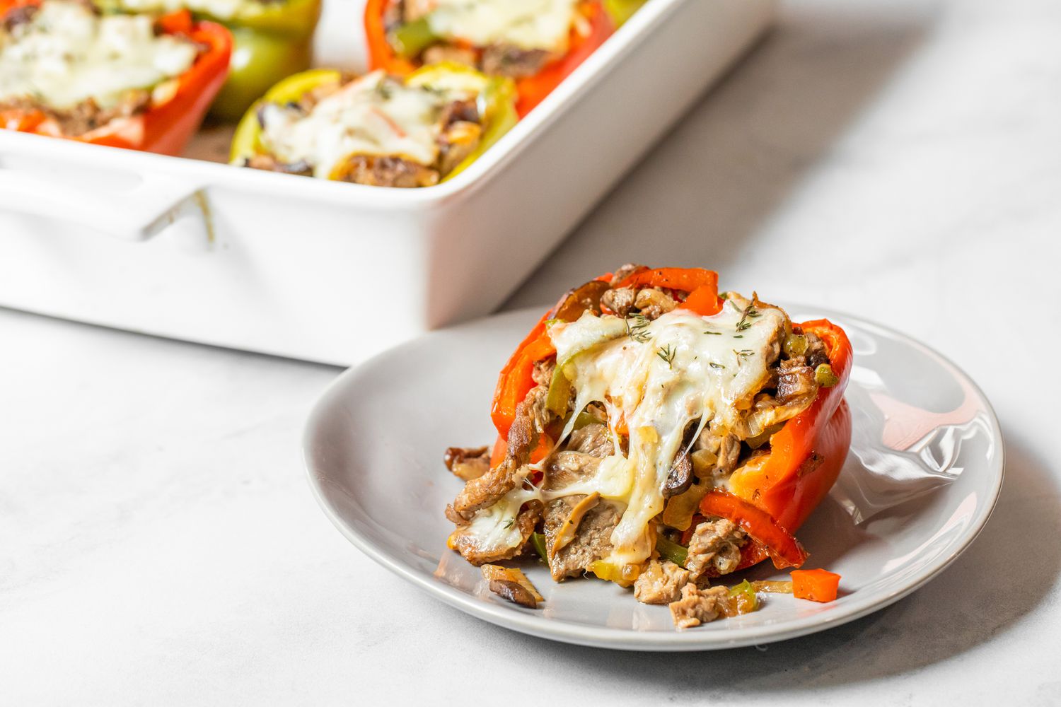 Philly Cheesesteak Stuffed Peppers on a Plate Next to a Casserole Dish with More Stuffed Peppers