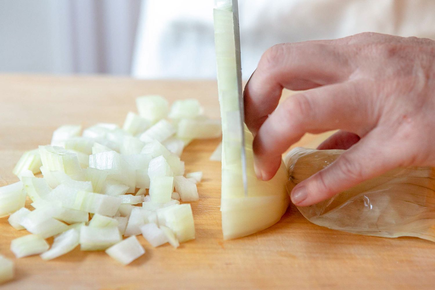 Curled Fingers Moved Towards the End of the Onion as the Knife Cuts Continues Cutting Cross-wise for How to Chop an Onion