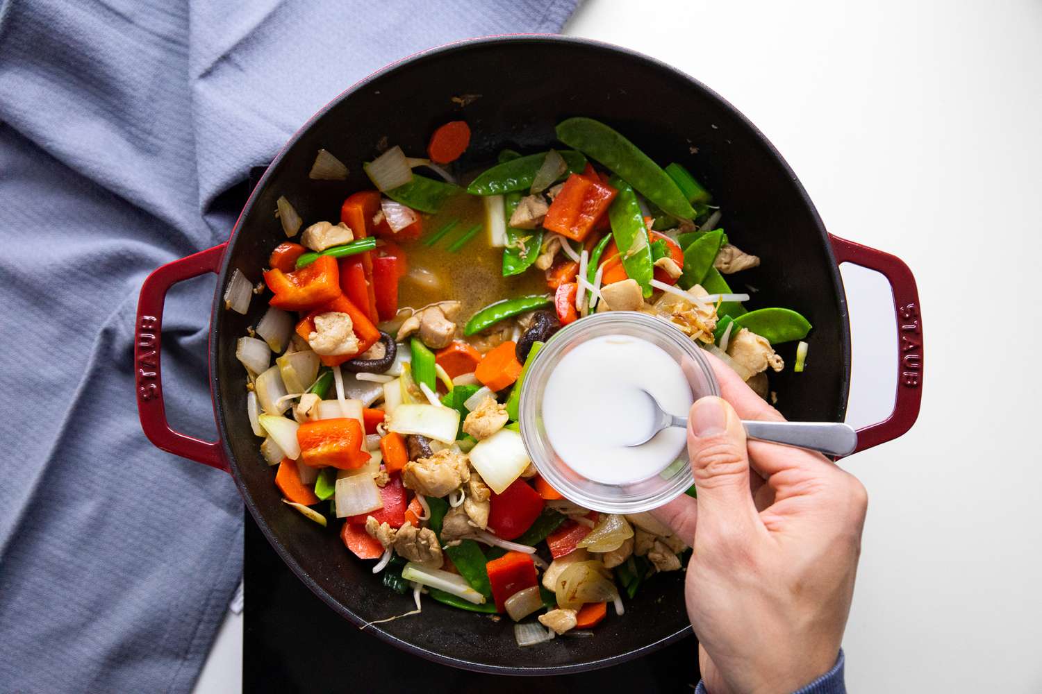 Small Bowl With Cornstarch Slurry Above the Wok on the Portable Burner Next to a Blue Kitchen Towel