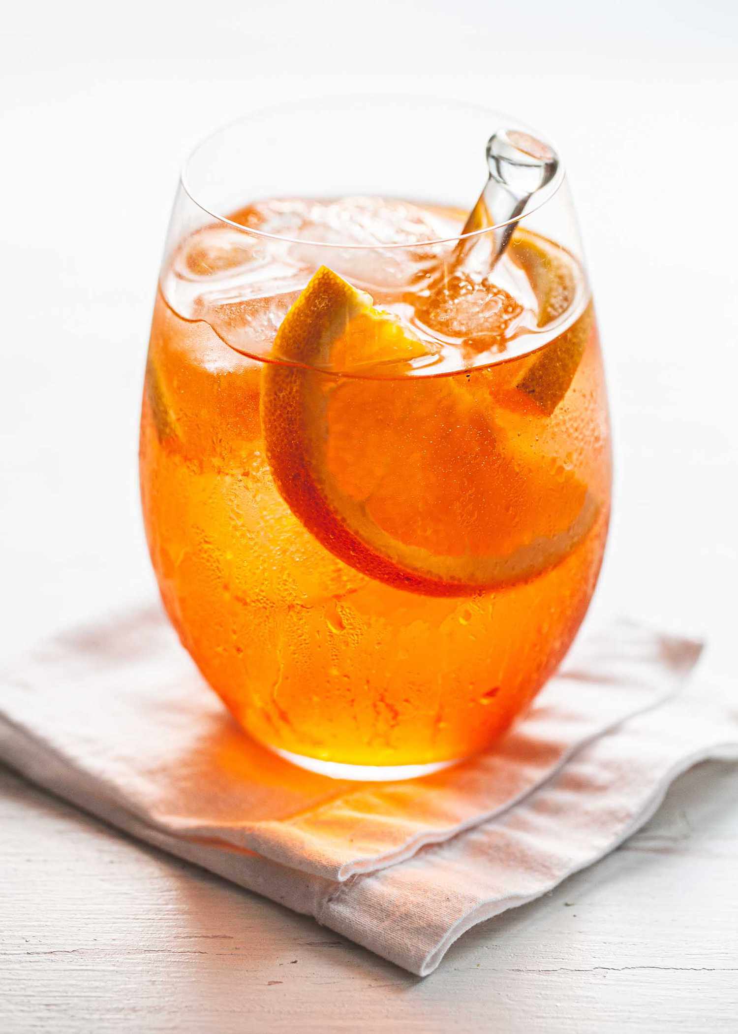 Aperol spritz cocktail in a wine glass with ice, orange slices and a stir stick.