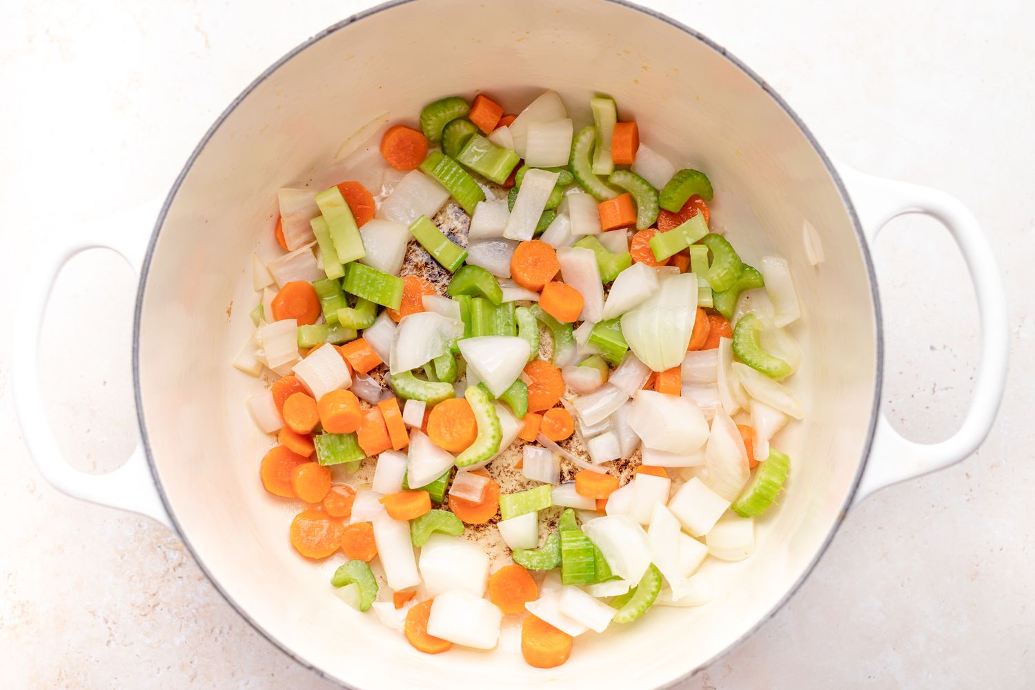 A dutch oven with carrots, celery, and onion inside to make a butternut squash soup recipe.
