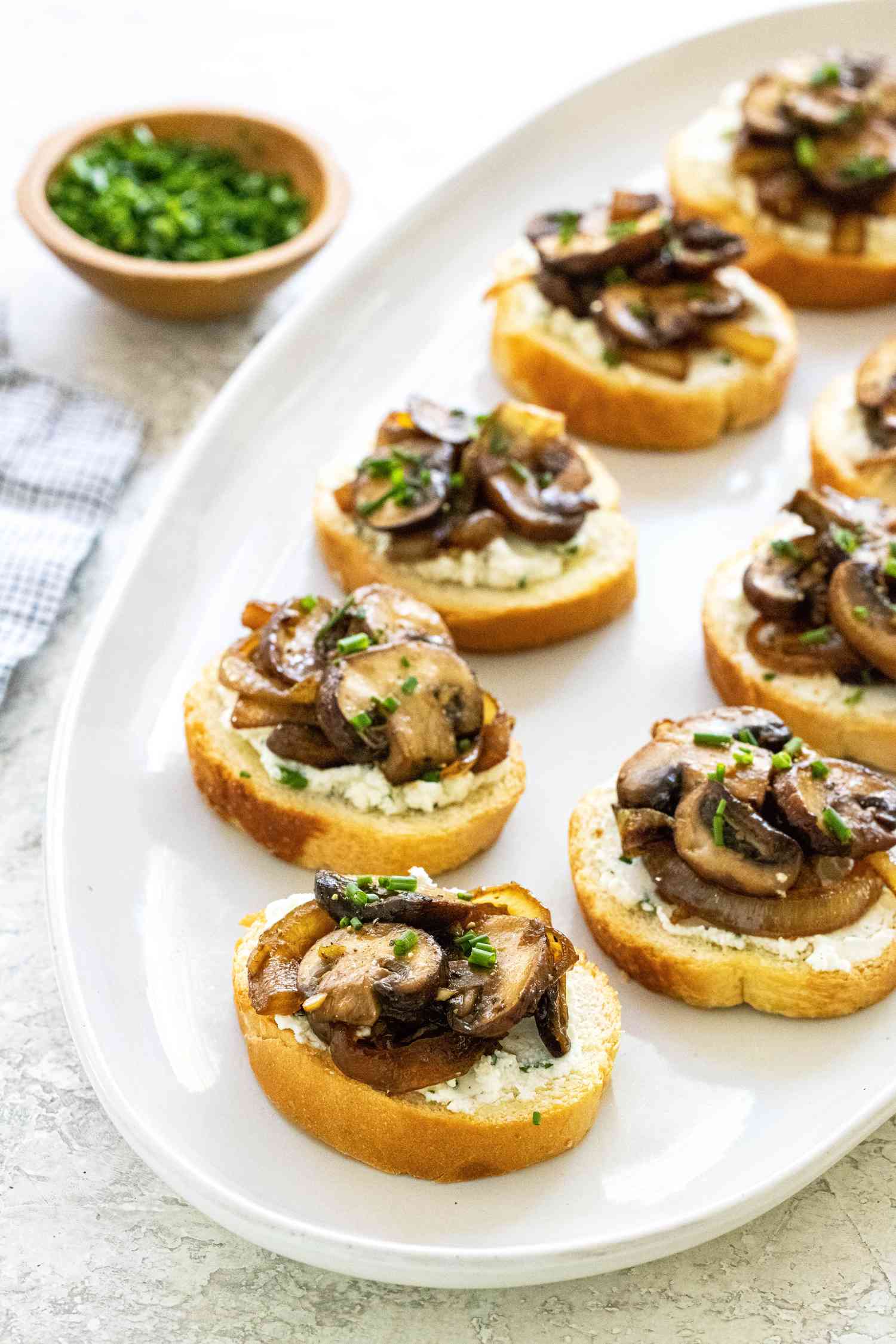 Mushroom and caramelized onion crostini on a white platter.