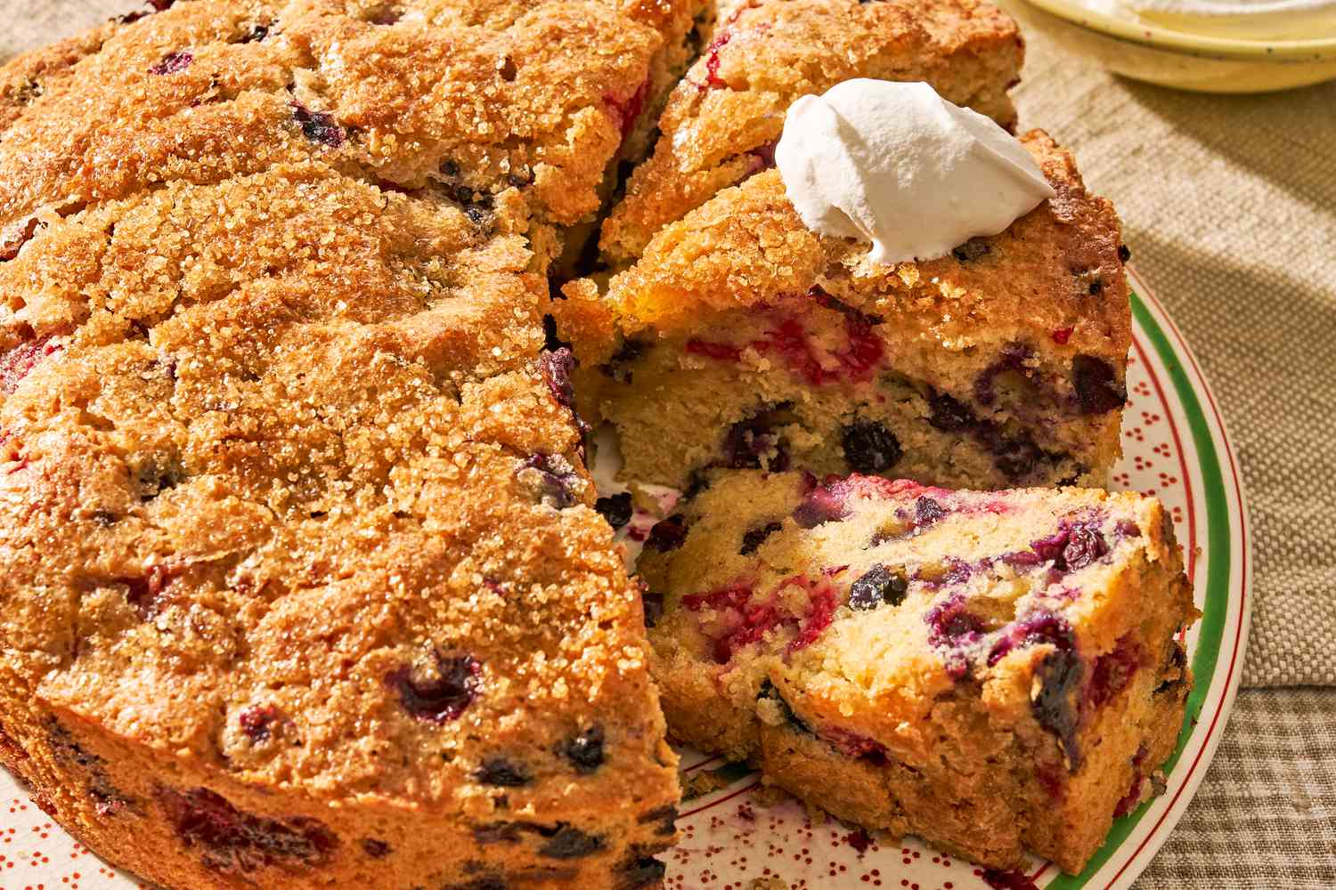 berry buckle (some of cut into slices and topped with whipped cream) on a plate at a cozy table setting (cottagecore vibes)