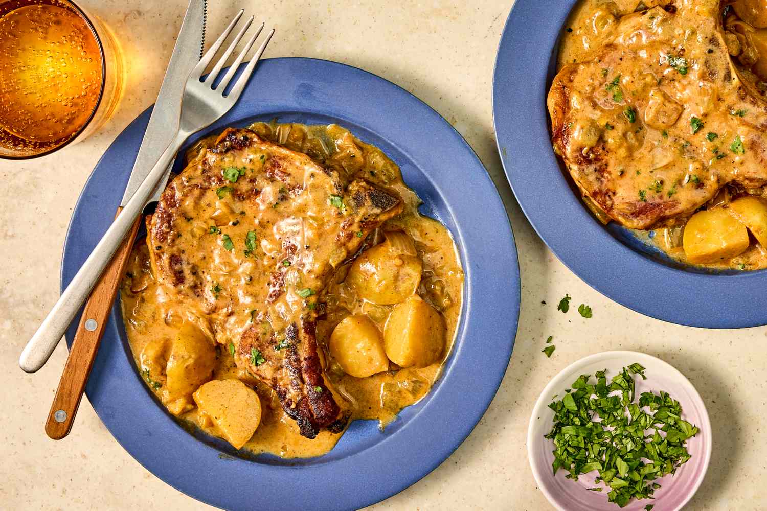 Plates of cowboy pork chops with creamy sauce and potatoes garnished with chopped herbs